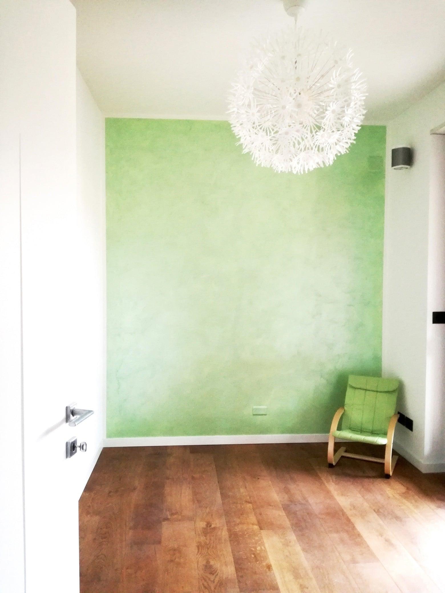 Stanza con parete verde, parquet e lampada a sospensione bianca