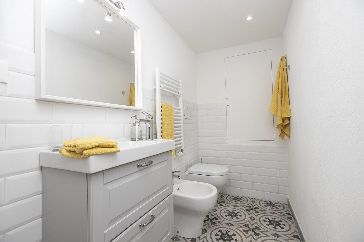 Bagno bianco con pavimento decorato e tessili gialli